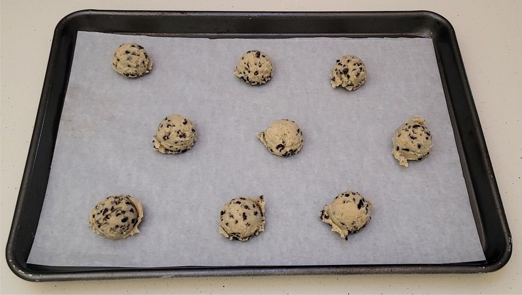 cocoa nib cookies scooped onto a sheet pan lined with parchment paper to prepare for baking