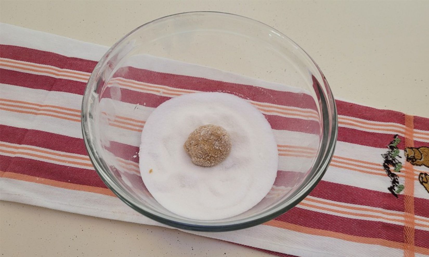 rolling ginger cookie dough balls in granulated sugar before baking