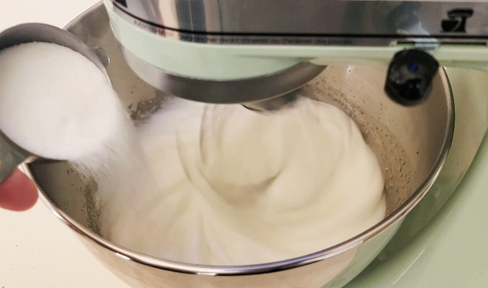 pouring granulated sugar into egg whites while whipping in a stand mixer