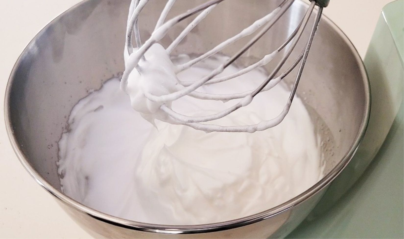 mixer whip showing egg whites whipped to stiff peaks