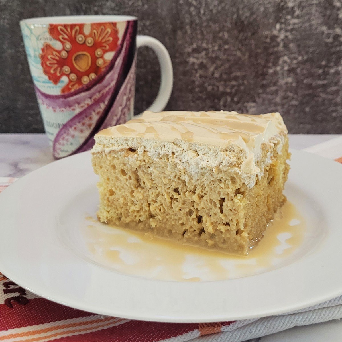 slice of coffee Tres Leches cake on a plate with coffee cup in background