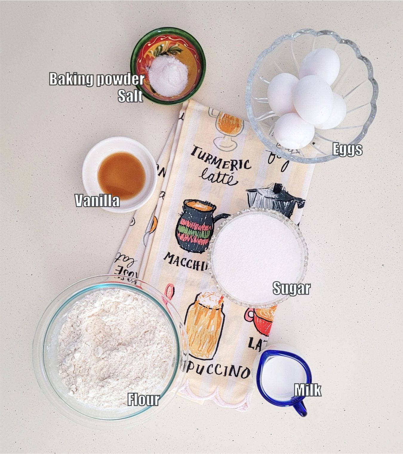 overhead view of ingredients needed to make sponge cake including flour, sugar, vanilla, milk, eggs, baking powder and salt