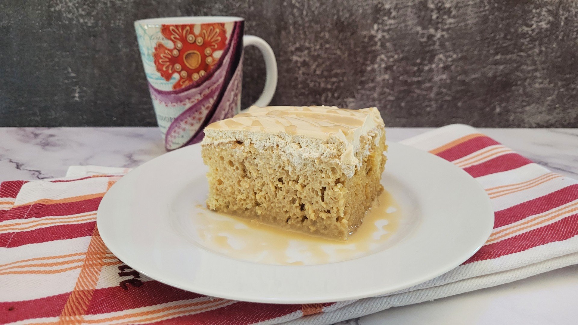 round plate with a slice of cake made with coffee Tres Leches recipe and a cup in the background