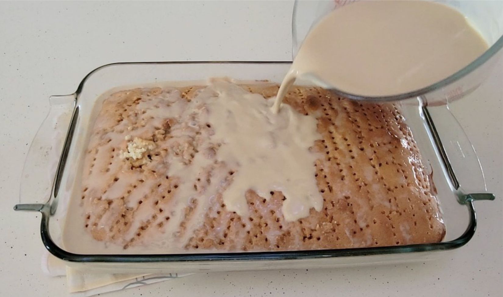 pouring coffee tres leches over sponge cake with holes poked in cake