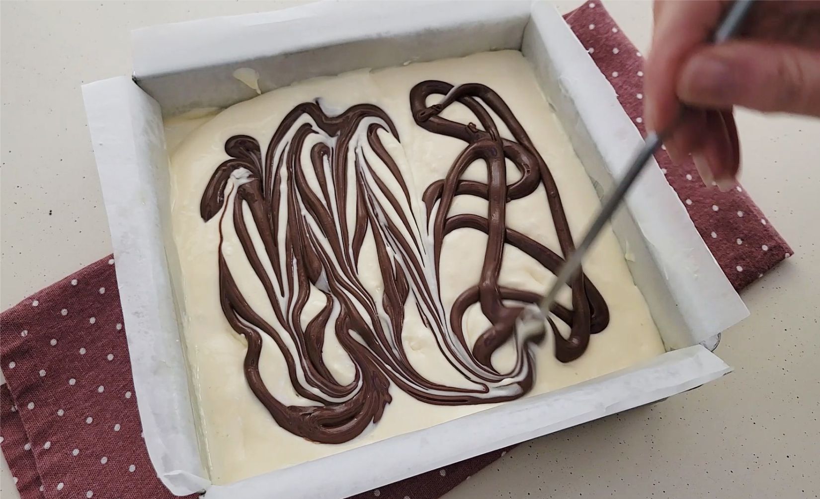 using a chop stick to make swirls in Nutella into cheesecake batter