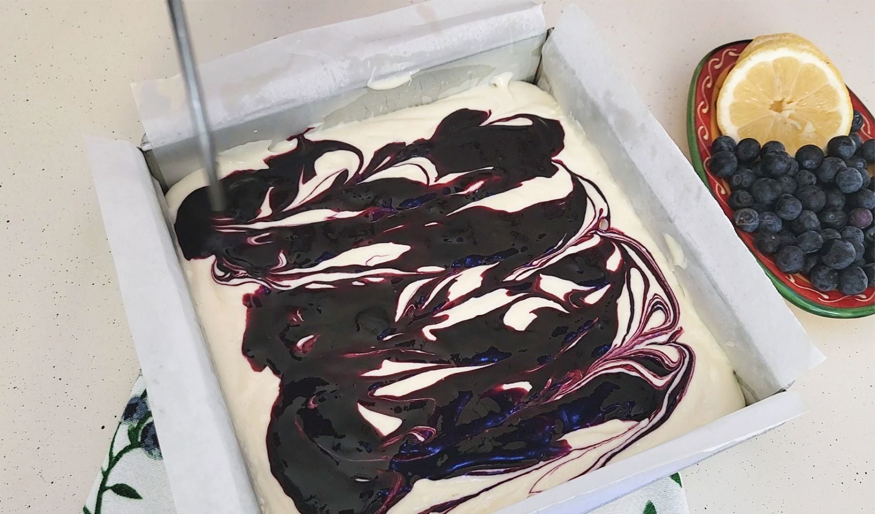 using a chopstick to swirl blueberry sauce into cheesecake batter to make dessert bars