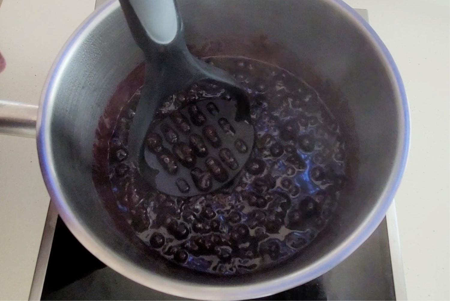 using a potato masher to smash blueberries in saucepan