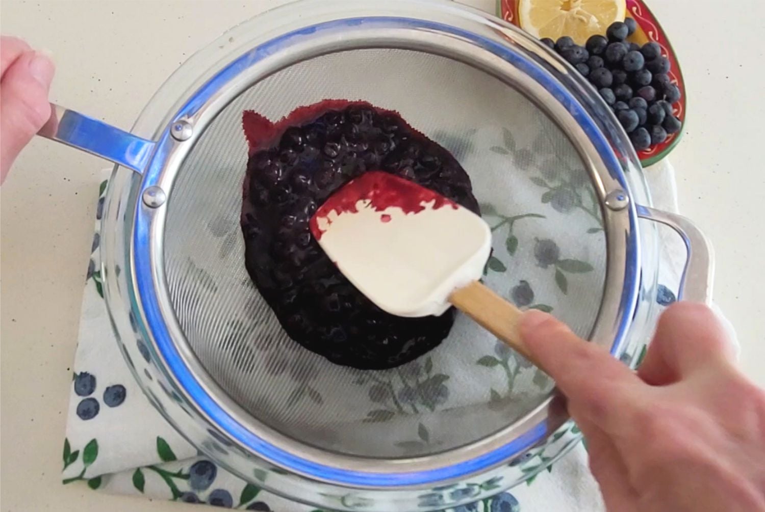 straining blueberries through a sieve to make sauce