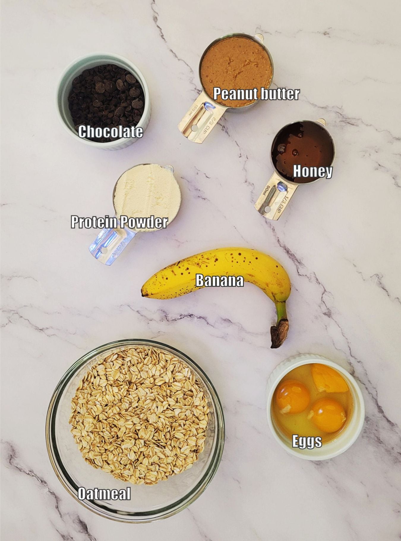 ingredients needed to make granola bars including oatmeal, eggs, honey, chocolate chips, protein powder, peanut butter and a banana