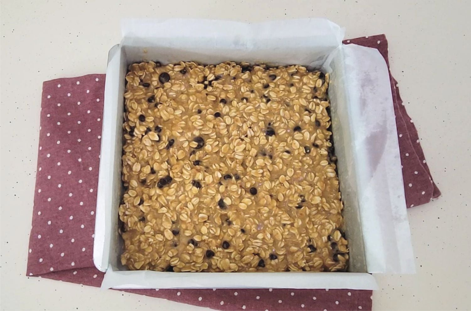protein granola bar dough recipe pressed into a square pan to prepare for baking